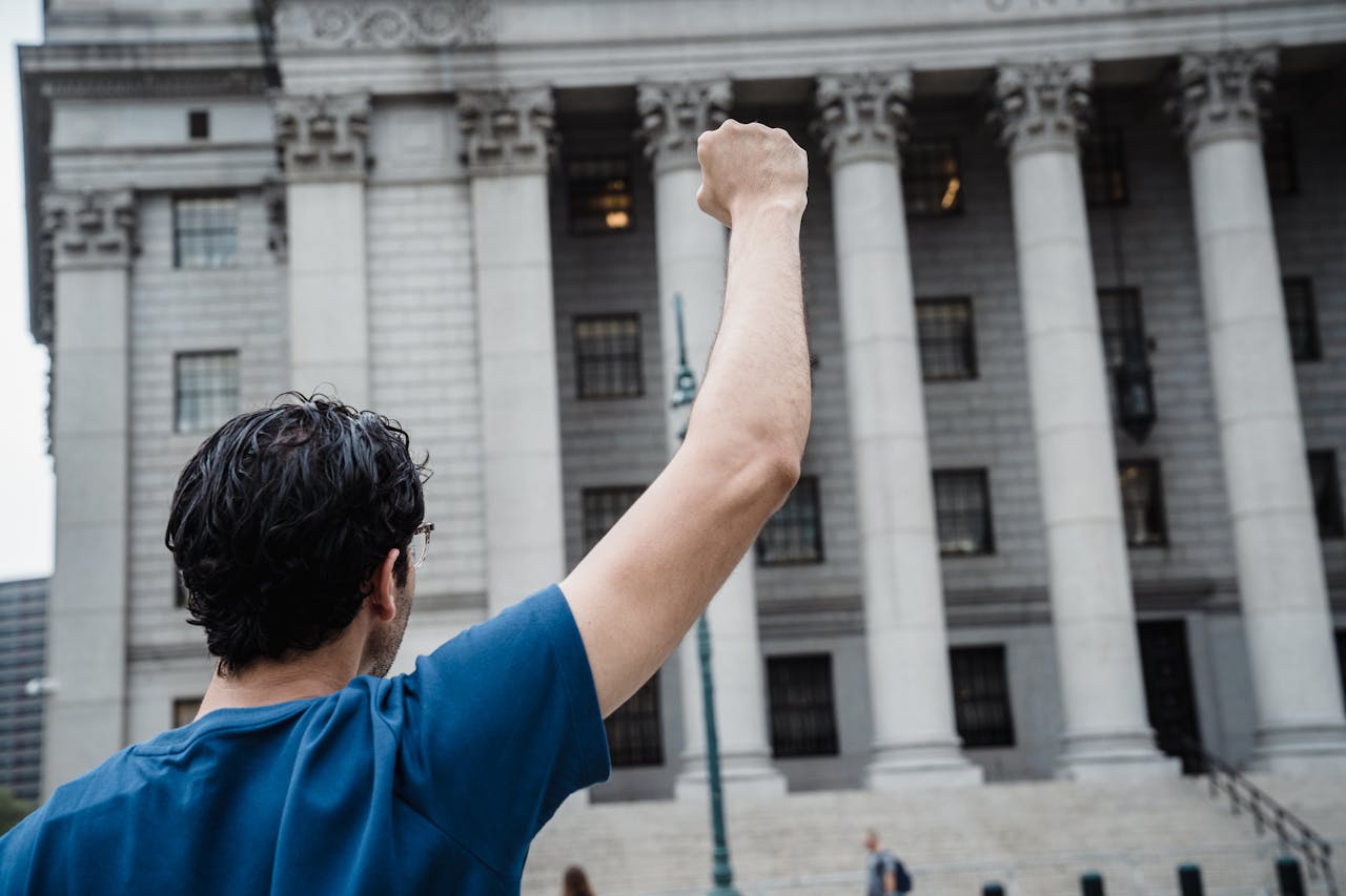 A person stands with raised fist in front of a classic architectural building, symbolizing activism.